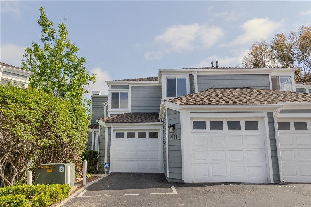 Gray two-story California townhouse with white garage, driveway, and green trees.
