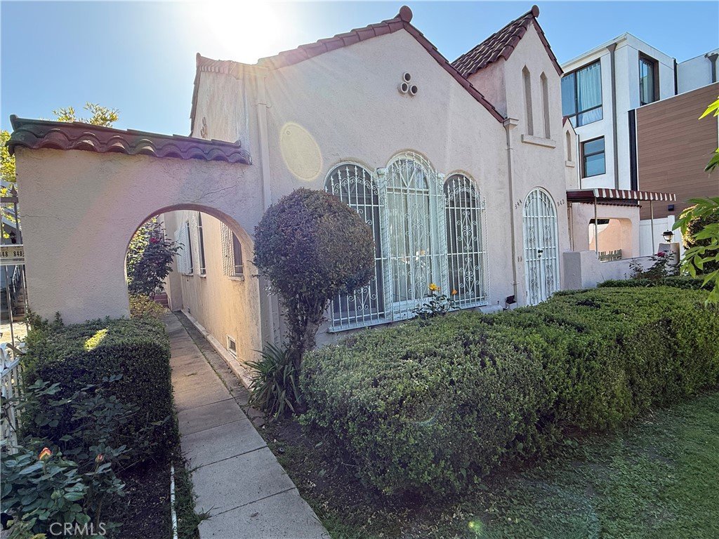 Pink California house with arched windows, white bars, and green hedges.