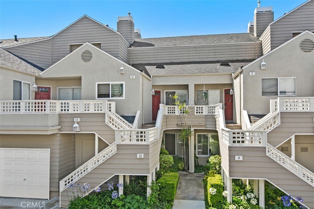 Modern California townhouse complex with beige and gray siding, red doors, balconies, and landscaped greenery.
