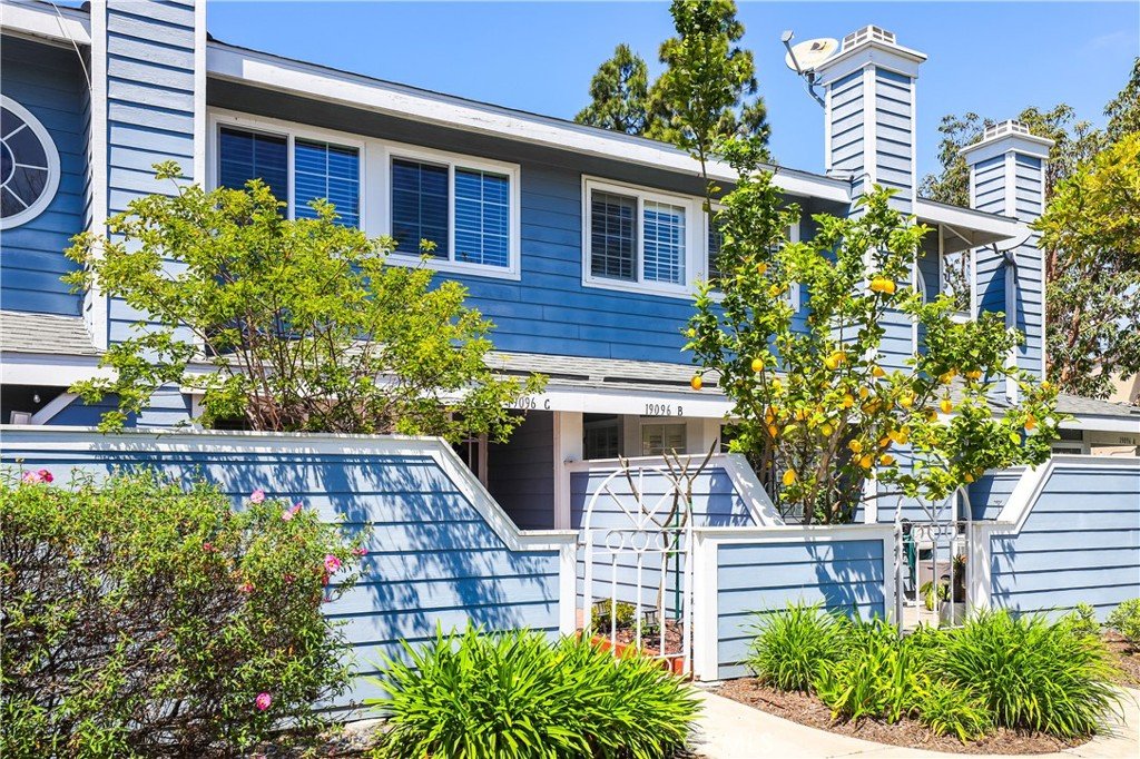 Blue California townhouse with white trim, large windows, chimneys, and green plants in front yard.