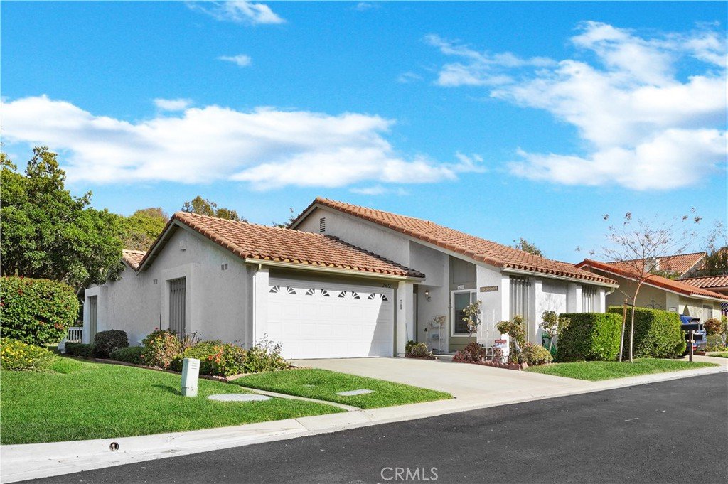 Single-story California house with white stucco walls, red-tiled roof, and green lawn.
