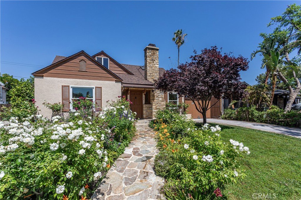 California house with stone chimney and garden of white flowers and green plants.