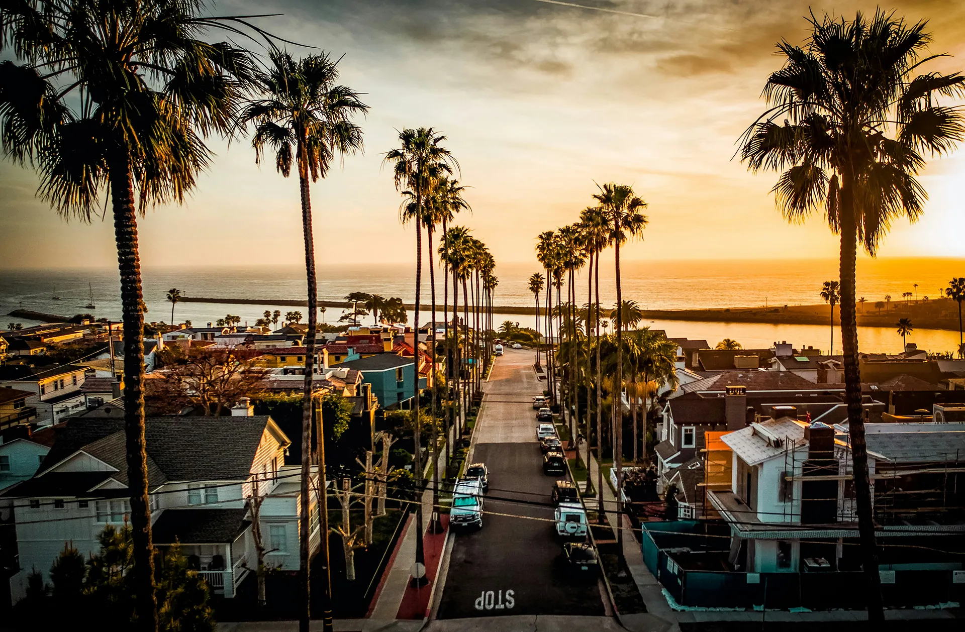 Serene California coastal street at sunset with palm trees, ocean view, and warm golden light on houses.