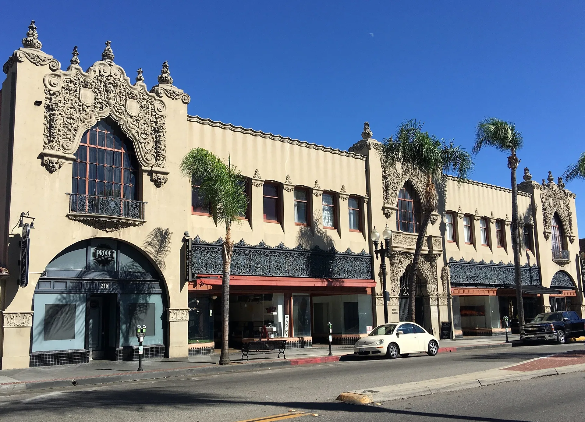 California building with stucco details, arched windows, and palm trees along the street.